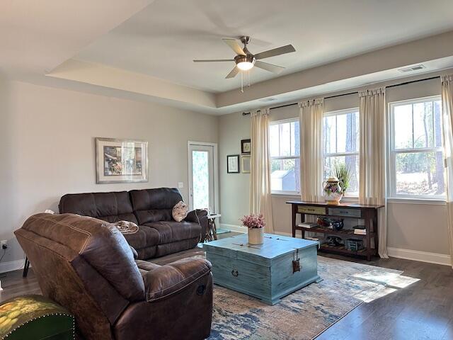 living room featuring dark wood-style floors, baseboards, and a tray ceiling