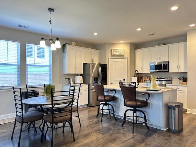 kitchen with stainless steel appliances, white cabinets, light countertops, and a center island with sink