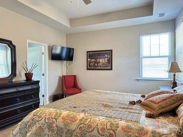 bedroom with ceiling fan, a raised ceiling, and visible vents