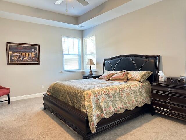 bedroom featuring a ceiling fan, a raised ceiling, light carpet, and baseboards