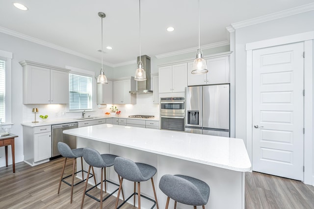 kitchen with wall chimney exhaust hood, a sink, light wood-style floors, decorative backsplash, and appliances with stainless steel finishes