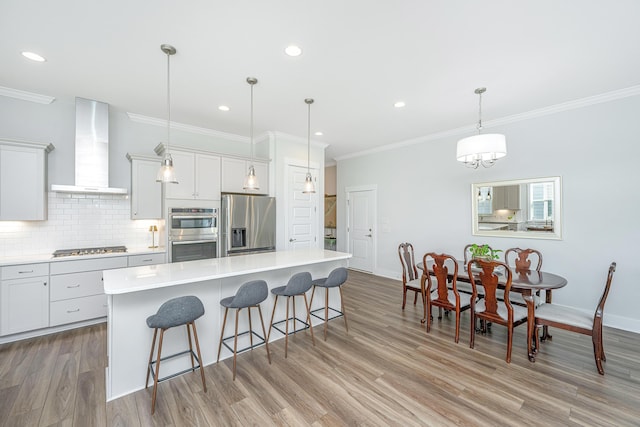 kitchen featuring a kitchen breakfast bar, ornamental molding, wall chimney exhaust hood, tasteful backsplash, and appliances with stainless steel finishes