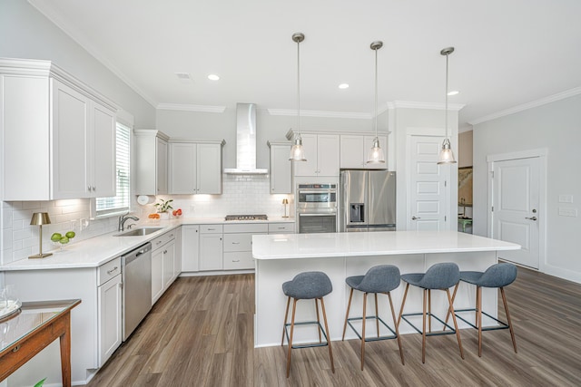 kitchen featuring a breakfast bar, wall chimney range hood, dark wood-type flooring, a center island, and appliances with stainless steel finishes