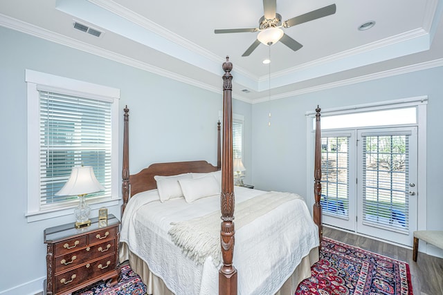 bedroom featuring wood finished floors, visible vents, access to outside, and a tray ceiling