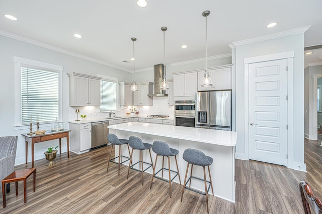 kitchen with wall chimney exhaust hood, stainless steel appliances, a sink, dark wood finished floors, and a kitchen bar