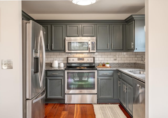 kitchen with dark hardwood / wood-style flooring, stainless steel appliances, gray cabinetry, and backsplash