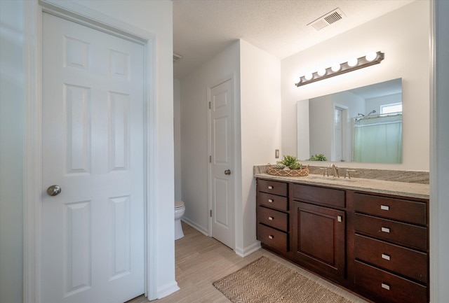 bathroom with wood-type flooring, vanity, a textured ceiling, and toilet