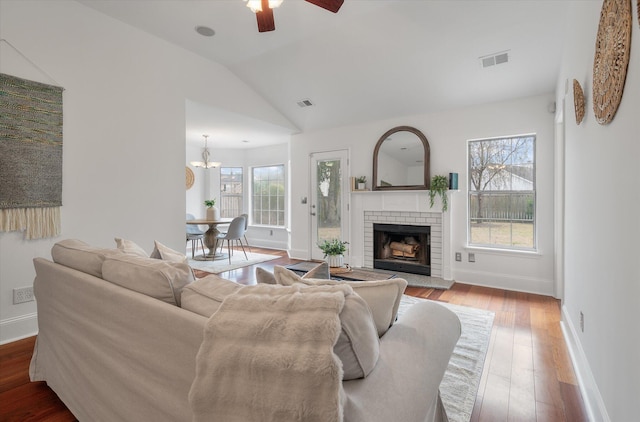 living room featuring a fireplace, hardwood / wood-style floors, ceiling fan with notable chandelier, and vaulted ceiling