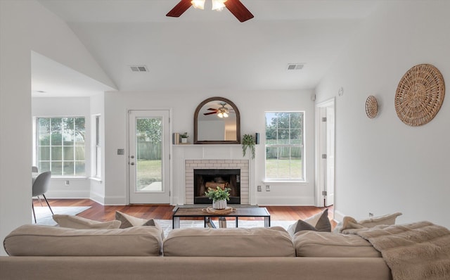 living room with a brick fireplace, ceiling fan, light wood-type flooring, and vaulted ceiling