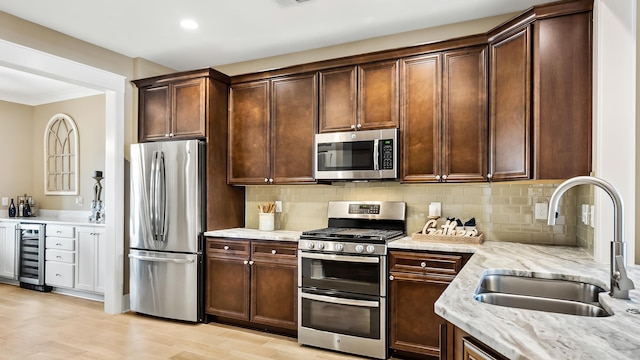 kitchen with appliances with stainless steel finishes, sink, light stone counters, backsplash, and beverage cooler