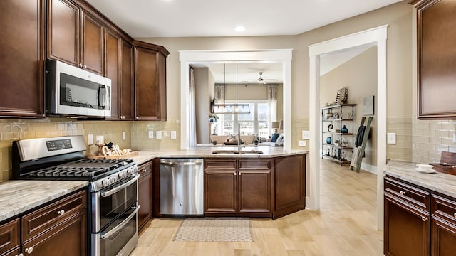 kitchen featuring backsplash, light hardwood / wood-style floors, light stone countertops, appliances with stainless steel finishes, and sink