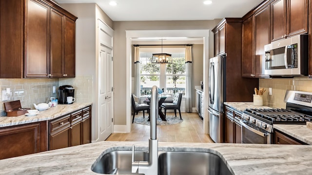 kitchen featuring appliances with stainless steel finishes, light hardwood / wood-style flooring, hanging light fixtures, backsplash, and a chandelier