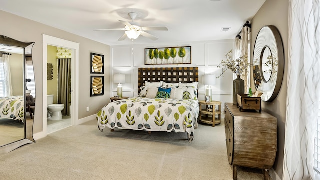 bedroom featuring light colored carpet, ensuite bath, and ceiling fan