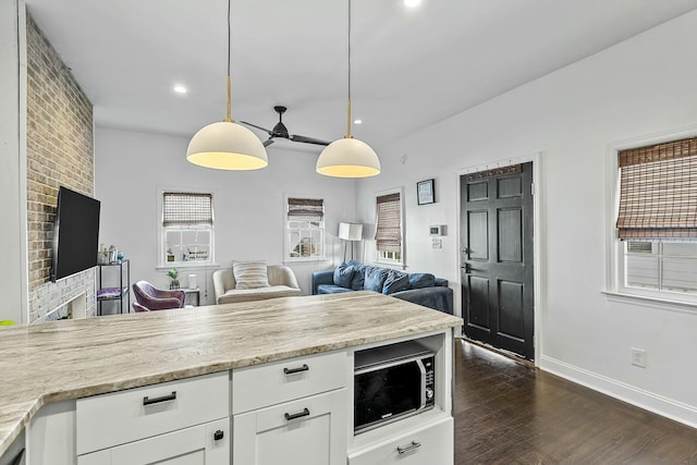 kitchen with hanging light fixtures, dark hardwood / wood-style floors, white cabinets, and light stone counters