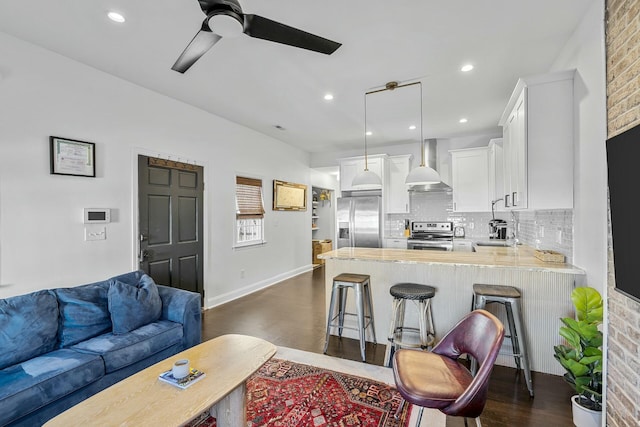 kitchen featuring a breakfast bar, white cabinetry, decorative light fixtures, stainless steel appliances, and wall chimney range hood