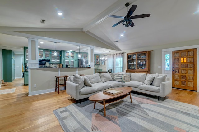 living area with vaulted ceiling with beams, light wood-style flooring, ceiling fan with notable chandelier, visible vents, and baseboards