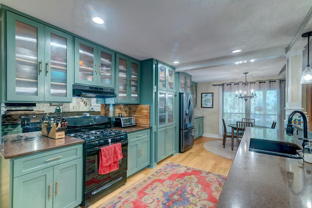 kitchen featuring gas stove, green cabinetry, under cabinet range hood, and stainless steel fridge