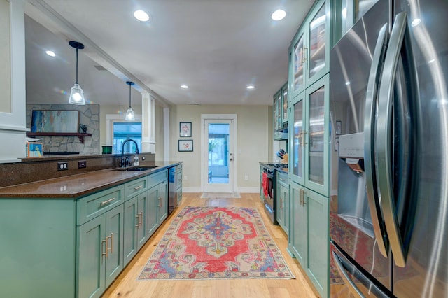 kitchen with stainless steel appliances, a sink, light wood-style flooring, and green cabinetry