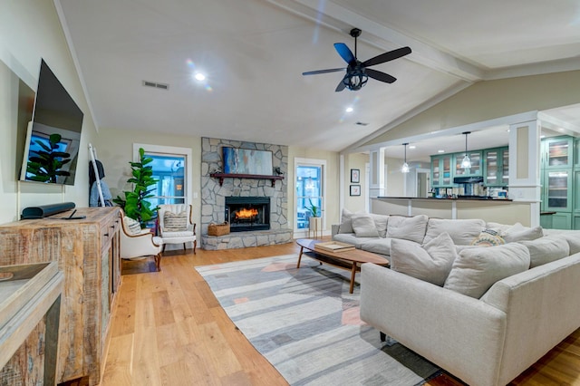 living room featuring vaulted ceiling with beams, a fireplace, visible vents, light wood-style flooring, and a ceiling fan