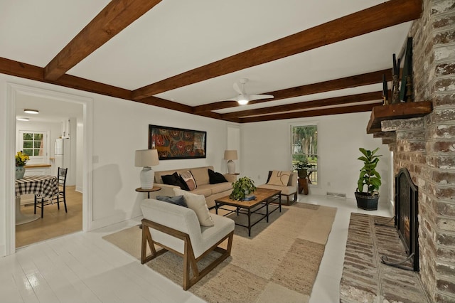 living room featuring ceiling fan, a fireplace, beamed ceiling, and light hardwood / wood-style flooring