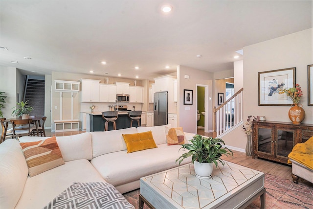 living room featuring recessed lighting, light wood-style flooring, stairs, and baseboards