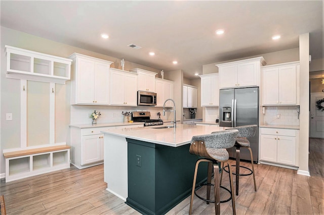 kitchen featuring visible vents, an island with sink, white cabinets, stainless steel appliances, and a sink