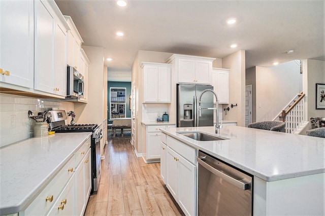 kitchen with a center island with sink, light wood-style flooring, a sink, stainless steel appliances, and white cabinetry