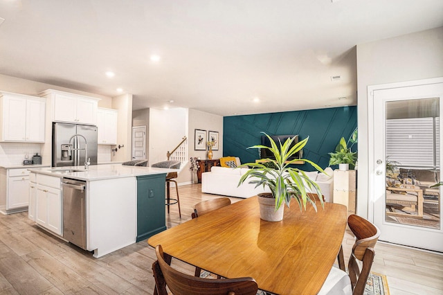 kitchen with an accent wall, light wood-type flooring, stainless steel appliances, white cabinetry, and a kitchen island with sink