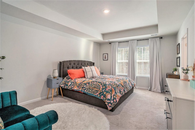 bedroom with light carpet, a tray ceiling, and baseboards