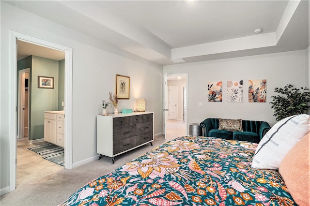 bedroom featuring a tray ceiling, baseboards, ensuite bathroom, and light carpet