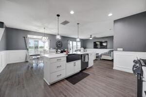 kitchen featuring black range with gas stovetop, dark wood-type flooring, open floor plan, hanging light fixtures, and a kitchen island with sink