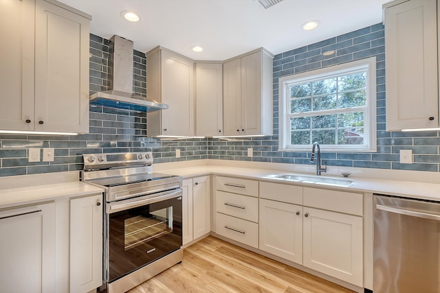 kitchen with sink, light hardwood / wood-style flooring, stainless steel appliances, decorative backsplash, and wall chimney exhaust hood