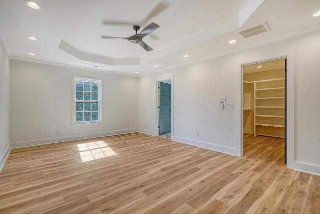 unfurnished bedroom with ornamental molding, a spacious closet, light hardwood / wood-style floors, and a tray ceiling