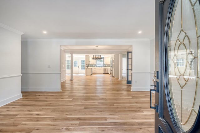 entryway with crown molding, a chandelier, decorative columns, and light hardwood / wood-style flooring