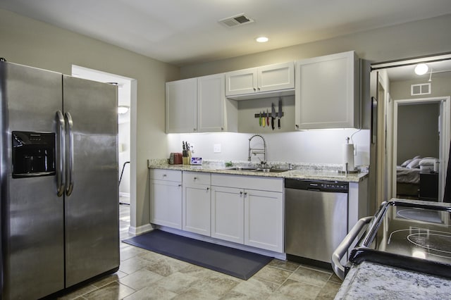 kitchen featuring stainless steel appliances, white cabinetry, light stone counters, and sink