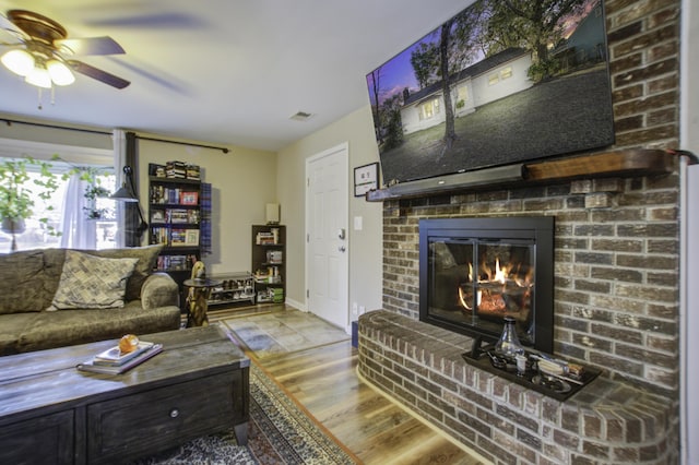 living room with ceiling fan, a brick fireplace, and light hardwood / wood-style flooring