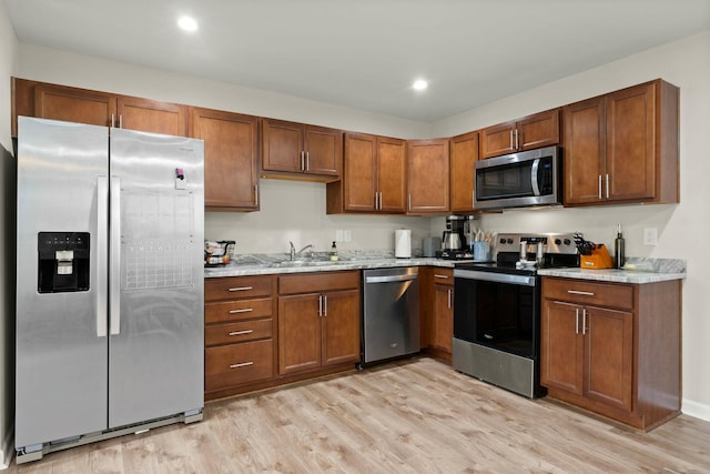 kitchen featuring light stone countertops, appliances with stainless steel finishes, light wood-type flooring, and sink