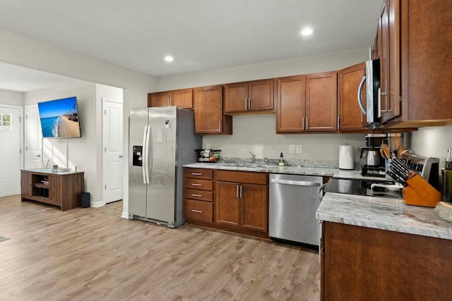 kitchen with light stone countertops, light hardwood / wood-style flooring, sink, and appliances with stainless steel finishes