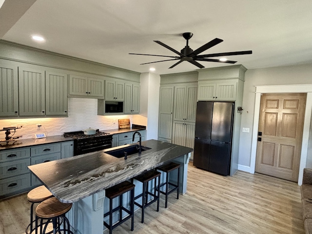 kitchen with a kitchen bar, ceiling fan, sink, black appliances, and light hardwood / wood-style floors