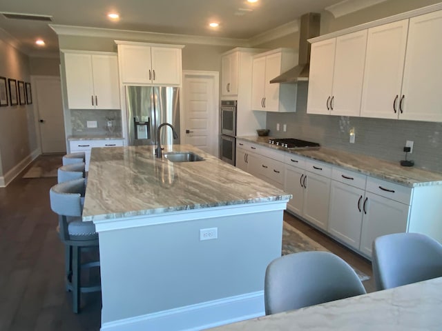 kitchen featuring sink, white cabinets, wall chimney range hood, stainless steel appliances, and a center island with sink