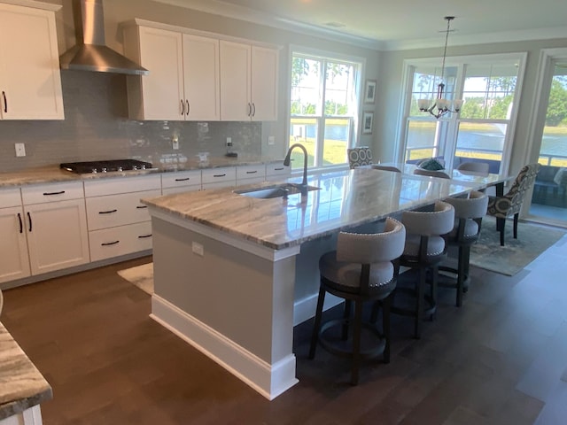 kitchen with white cabinets, stainless steel gas cooktop, a kitchen island with sink, sink, and wall chimney range hood