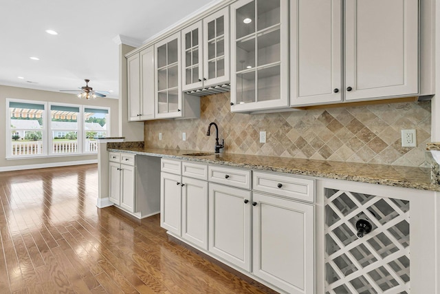 kitchen featuring tasteful backsplash, light stone countertops, dark hardwood / wood-style flooring, ceiling fan, and ornamental molding