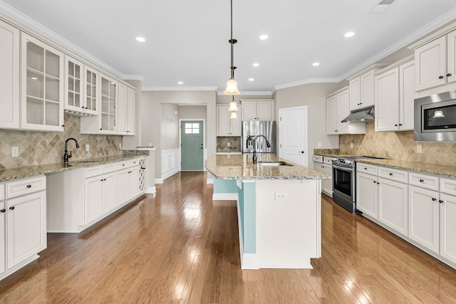 kitchen featuring an island with sink, stainless steel appliances, light wood-type flooring, decorative light fixtures, and sink