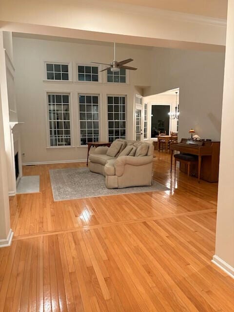 living room featuring light wood-style floors, a fireplace with flush hearth, baseboards, and ceiling fan