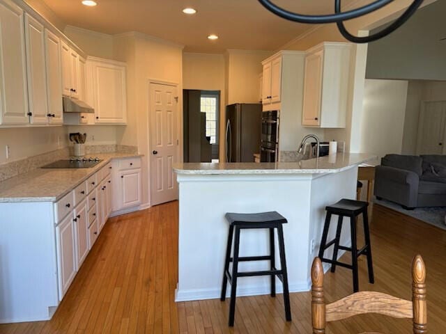 kitchen featuring a breakfast bar area, a peninsula, white cabinetry, under cabinet range hood, and black appliances