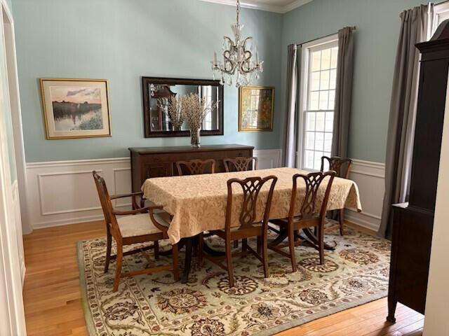 dining room with crown molding, a chandelier, light wood finished floors, and a wainscoted wall
