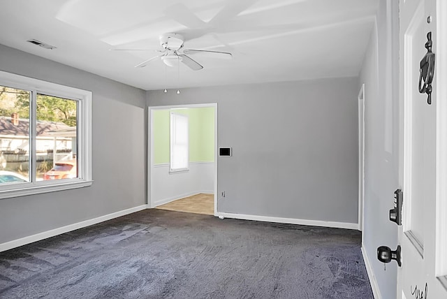 empty room with ceiling fan, a healthy amount of sunlight, and dark carpet