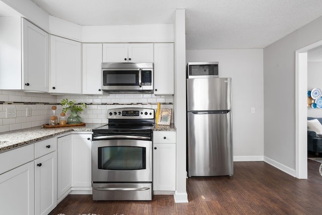 kitchen featuring appliances with stainless steel finishes, dark wood-type flooring, white cabinets, light stone countertops, and decorative backsplash