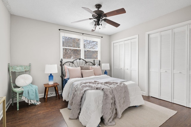 bedroom with ceiling fan, a textured ceiling, multiple closets, and dark hardwood / wood-style floors