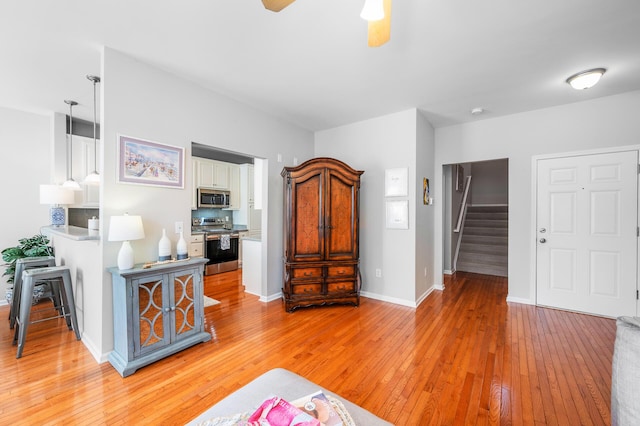 living area with a ceiling fan, baseboards, stairway, and light wood finished floors